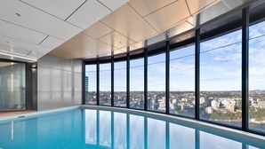 Une piscine intérieure moderne dotée de grandes baies vitrées offrant une vue sur la ville.