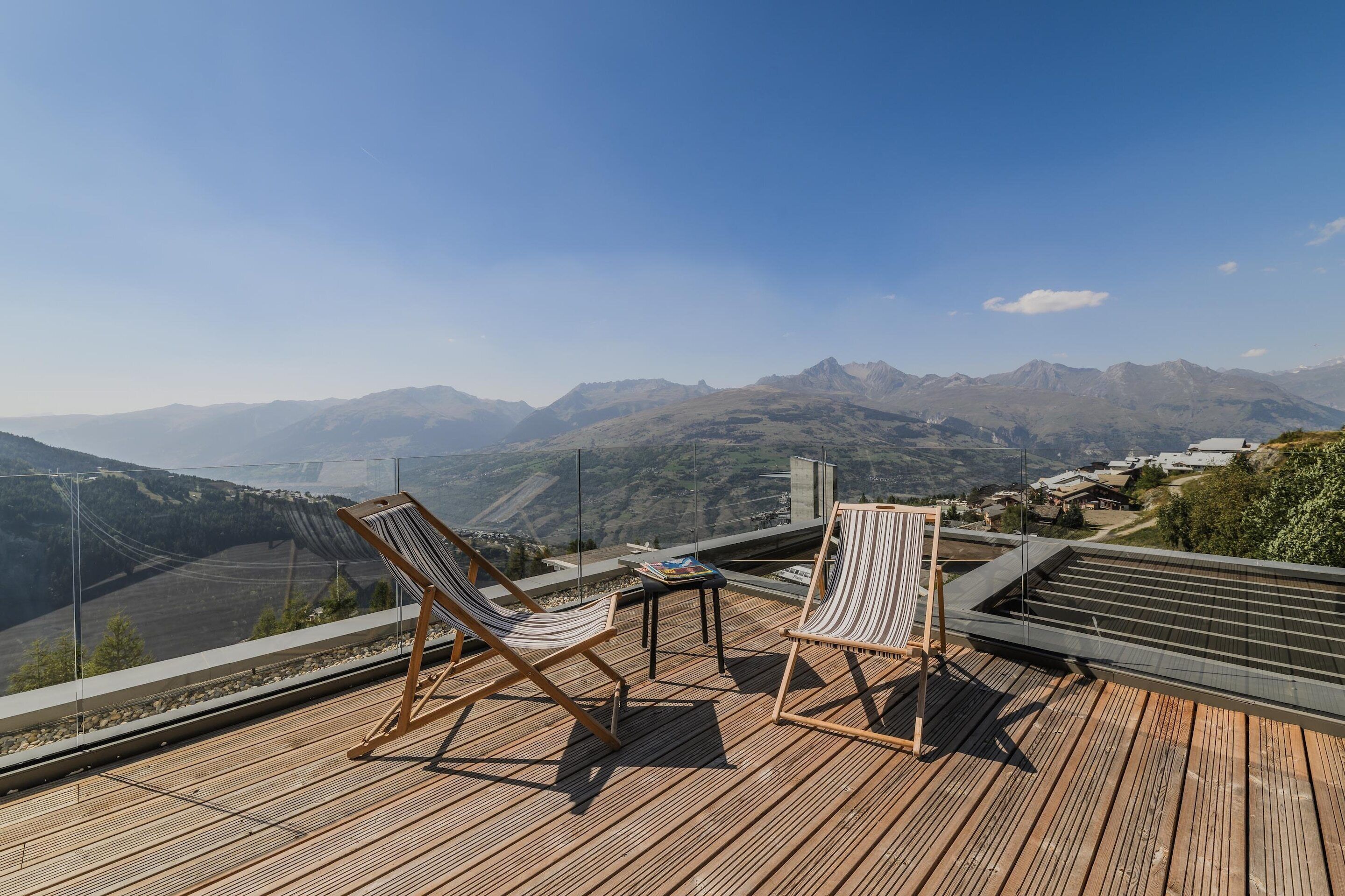 A wooden deck with two striped lounge chairs and a small table, overlooking a mountainous landscape.