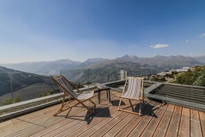 Une terrasse en bois avec deux chaises longues à rayures et une petite table, offrant une vue sur un paysage montagneux.