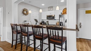 Una cocina moderna con muebles blancos, una isla de madera con taburetes altos e iluminación colgante.