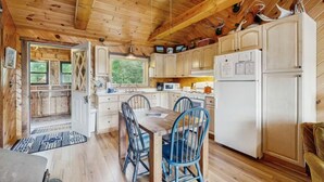 A wooden cabin interior with a dining area, kitchen, and a view of the outdoors.