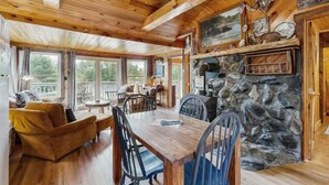 A cozy cabin interior with a stone fireplace, wooden dining table, and comfortable seating.