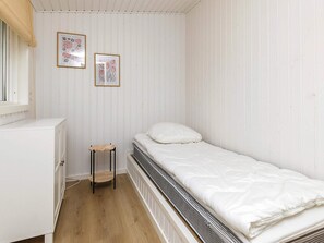 A small, white room with a bed, a radiator, a small wooden stool, and two framed pictures on the wall. - 4 Star Holiday Home in Dannemare (Dannemare)