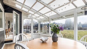 Une véranda avec une table ronde, des chaises et un vase de fleurs.