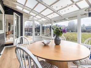 A conservatory with a round table, chairs, and a vase of flowers. - 4 Star Holiday Home in Dannemare (Dannemare)