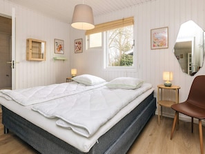 A bedroom with a bed, bedside lamps, a chair, a window, and a mirror. - 4 Star Holiday Home in Dannemare (Dannemare)