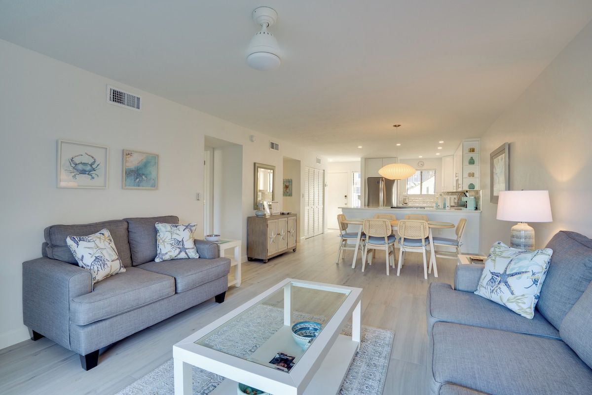 A modern living room with a grey sofa, a glass coffee table, and a dining area with a white table and chairs.