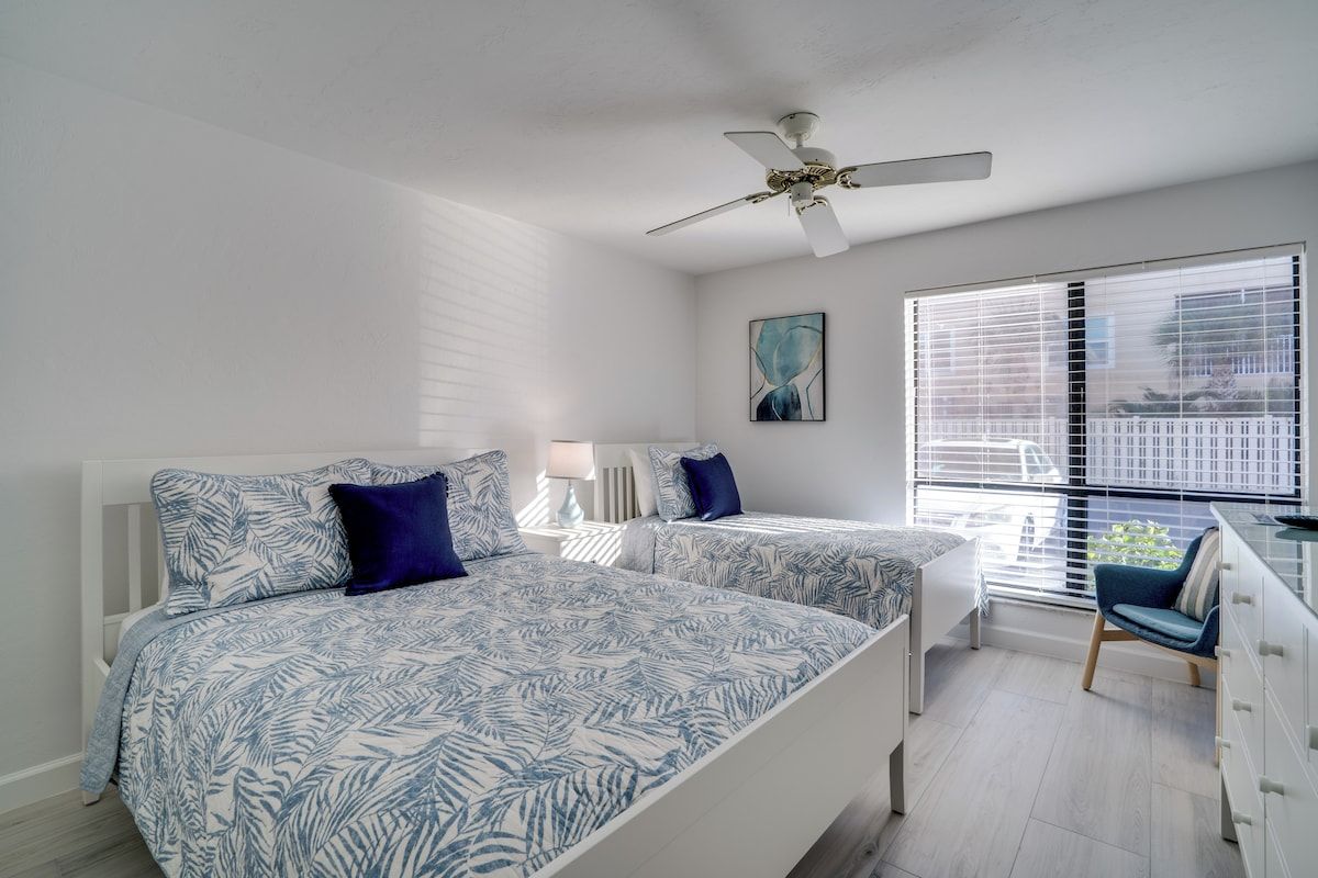 A bedroom with two beds, a ceiling fan, a window with blinds, and a chair.