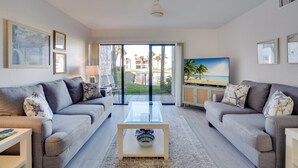 Uma sala de estar moderna com dois sofás cinzas, uma mesa de centro de vidro e uma TV sobre um móvel.
