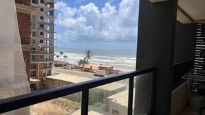 A balcony with a view of the beach and ocean, a brick building, and a tiled wall. - Apartment across from the beach for millionaires. (Ilhéus)