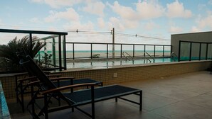 A rooftop pool area with lounge chairs and a glass enclosure overlooking the ocean. - Apartment across from the beach for millionaires. (Ilhéus)