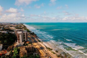 Vue aérienne d’une ville côtière avec une plage, des bâtiments et un ciel dégagé.
