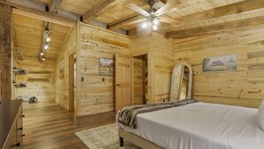 A wooden cabin bedroom with a bed, a ceiling fan, and a painting on the wall. - Hocking Hills: Timber Bear Lodge (McArthur)