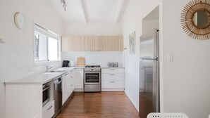 A modern kitchen with white cabinetry, a wooden floor, and stainless steel appliances. - Medona: Narrawallee Beach House (Narrawallee)