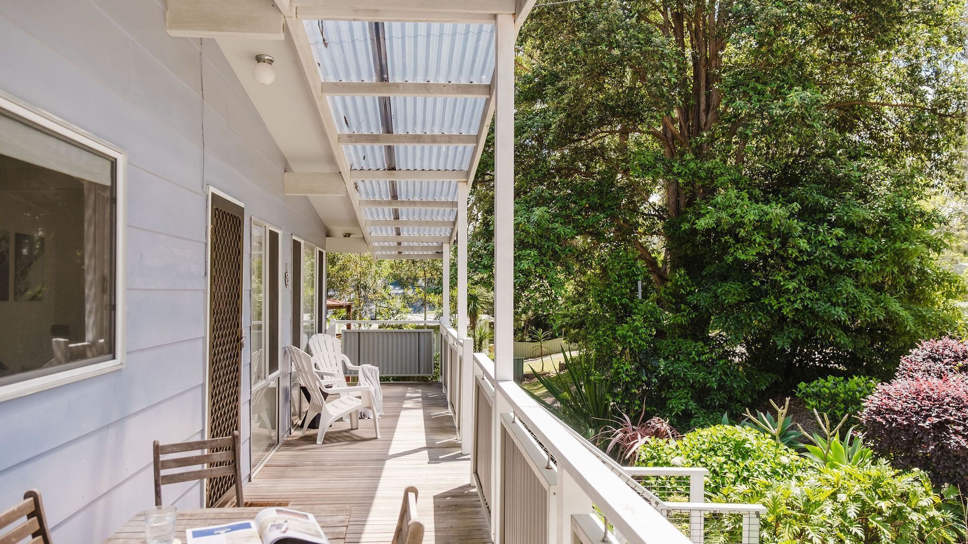 A covered outdoor area with a wooden deck, white chairs, and a table.