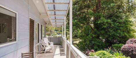 A covered outdoor area with a wooden deck, white chairs, and a table.