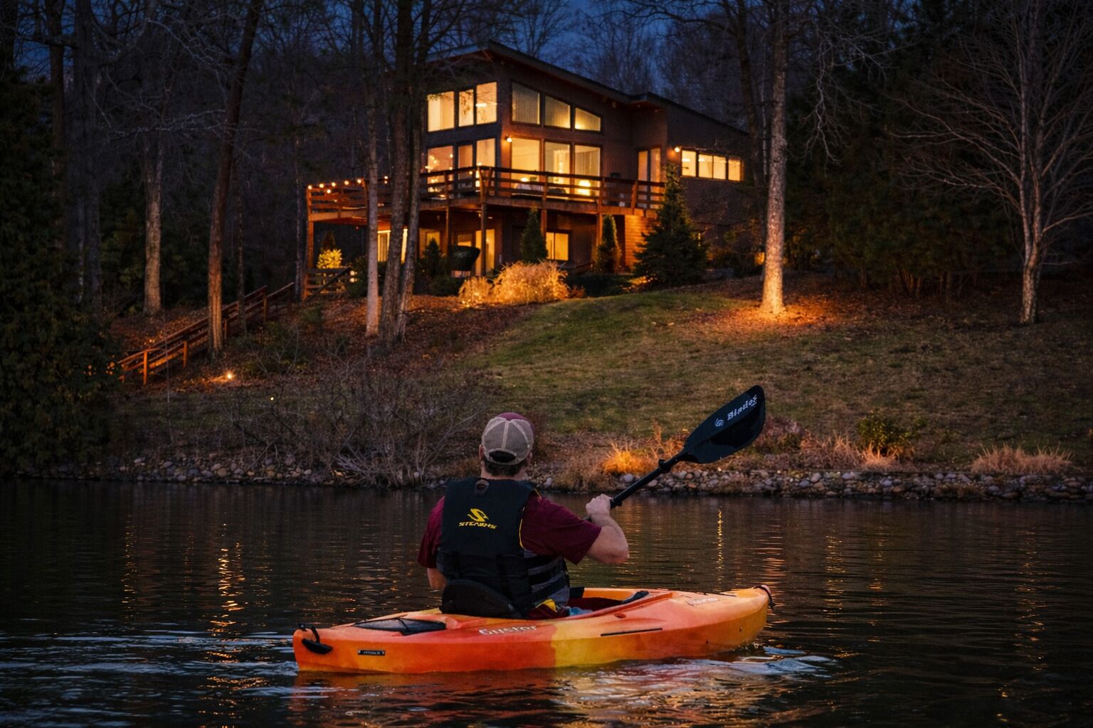 Una persona haciendo kayak en un cuerpo de agua con una casa al fondo.