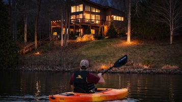 Una persona haciendo kayak en un cuerpo de agua con una casa al fondo.