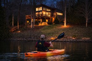 A person kayaking on a body of water with a house in the background.