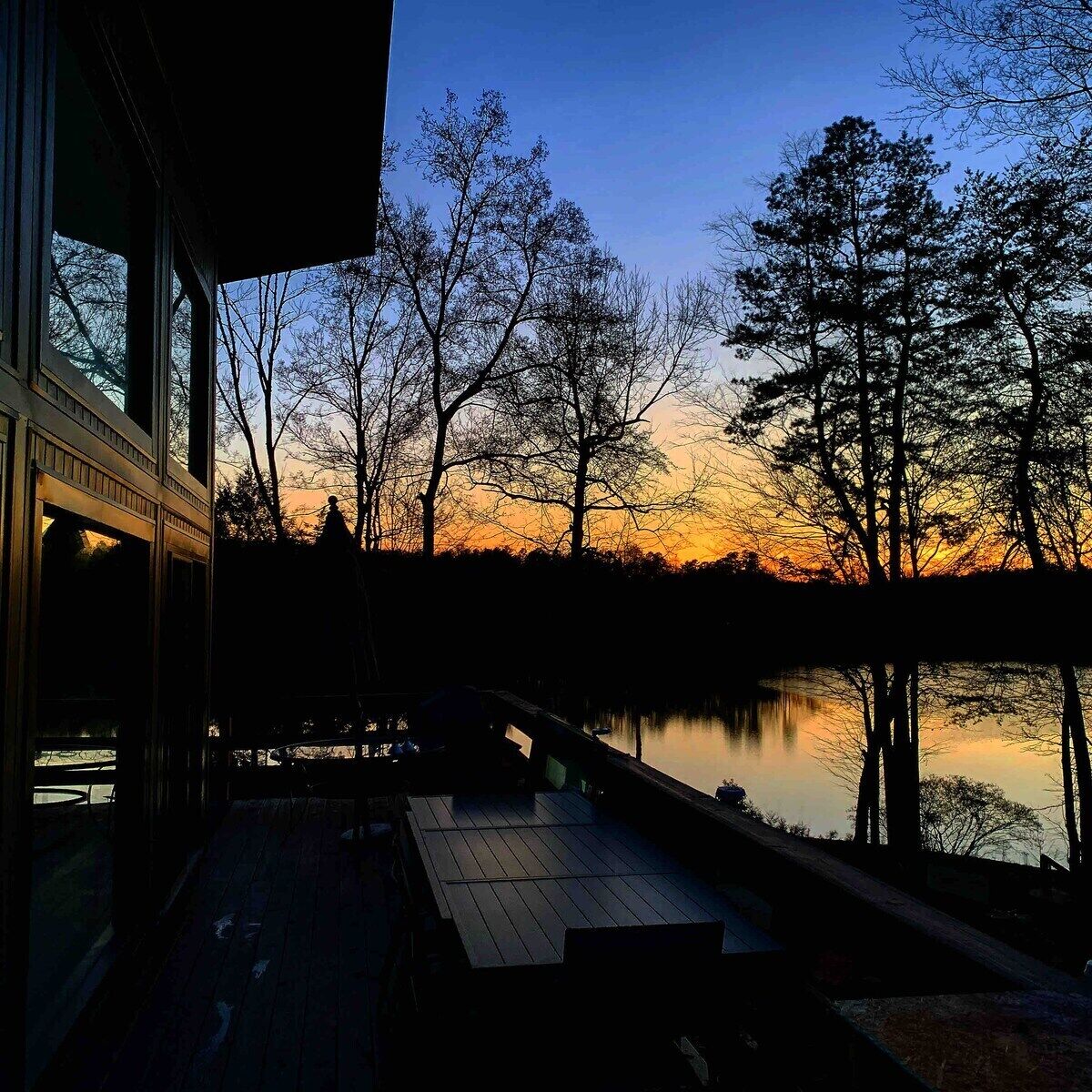 A lakeside view at dusk with a wooden deck and a building with large windows.