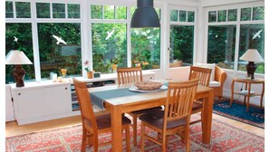 A dining area with a table, chairs, and a view of greenery through large windows. - Reetdachhaus in Burhave (Butjadingen)