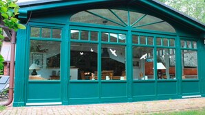 A conservatory with a green exterior, large windows, and a brick floor. - Reetdachhaus in Burhave (Butjadingen)