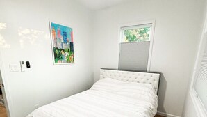 Ein Schlafzimmer mit einem Bett, einem Deckenventilator, einem Fenster mit Jalousien und einem an der Wand montierten Lichtschalter.