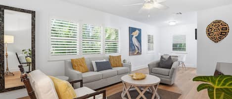 A modern living room with a sofa, armchair, and coffee table. There are decorative wall art pieces and a ceiling fan.