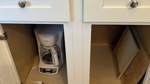 Eine Küche mit weißen Schränken, einer Kaffeemaschine und einer Holztür zu einem Schrank.