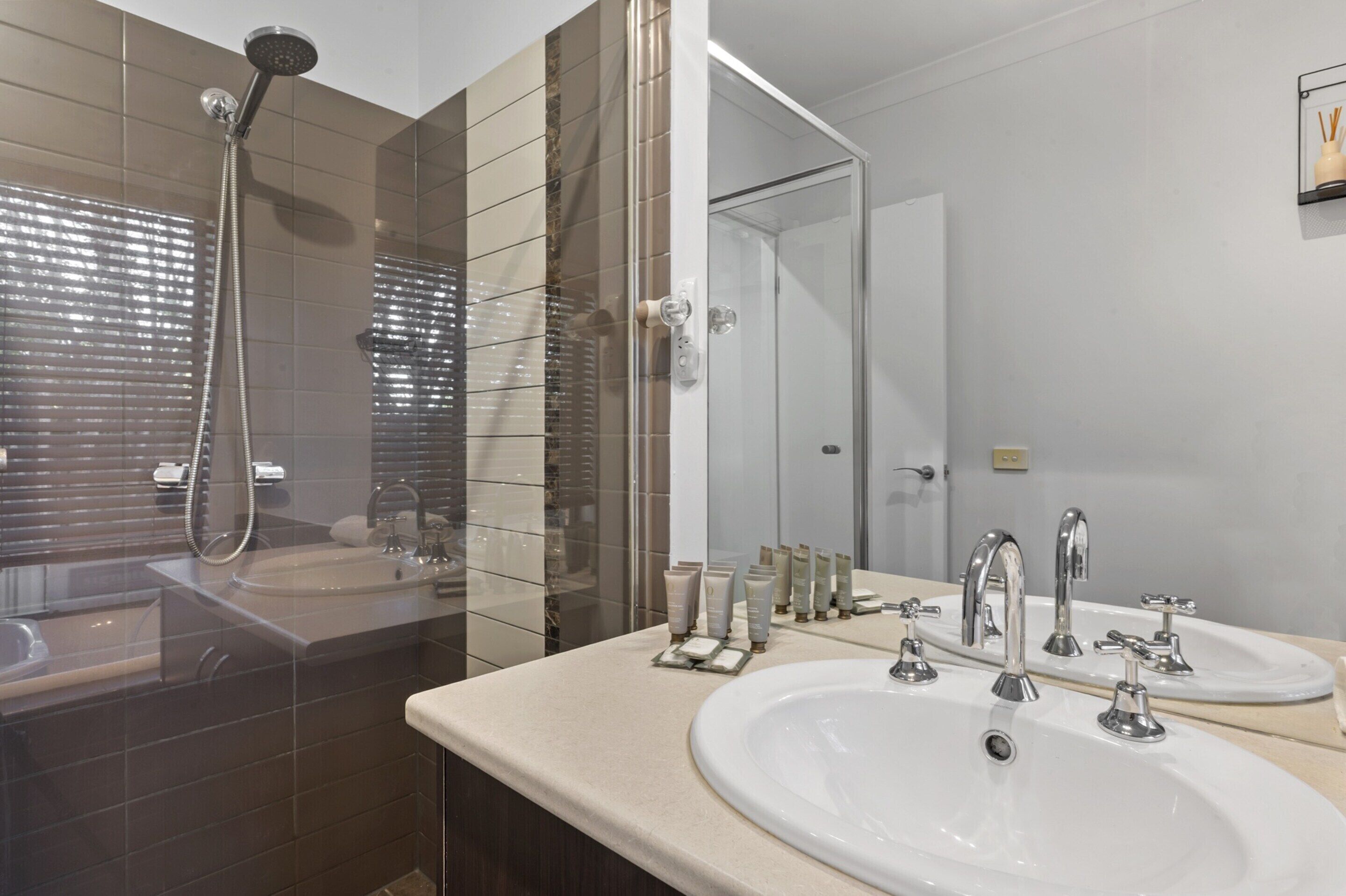 A modern bathroom with two sinks, a shower, and a glass-enclosed shower area.