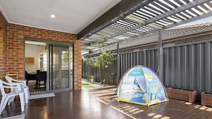 A covered outdoor patio with a wooden deck, a brick wall, and a colorful children's play tent. - Family Escape With Private Courtyard (Melbourne)