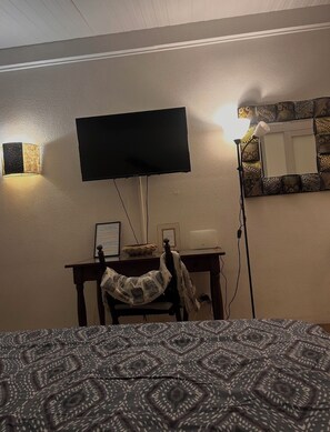 A room with a bed, a desk with a flat-screen TV, a lamp, and a patterned wall mirror. - Studio Kanao, paradise by the sea 600 m from Pointe Marin Ideal (Sainte-Anne)