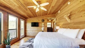 Une chambre dans un chalet en bois, avec un lit, un ventilateur de plafond, un téléviseur fixé au mur et une décoration représentant une tête de cerf.