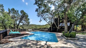 Une piscine entourée d’arbres, une terrasse en bois et un bâtiment au style rustique.