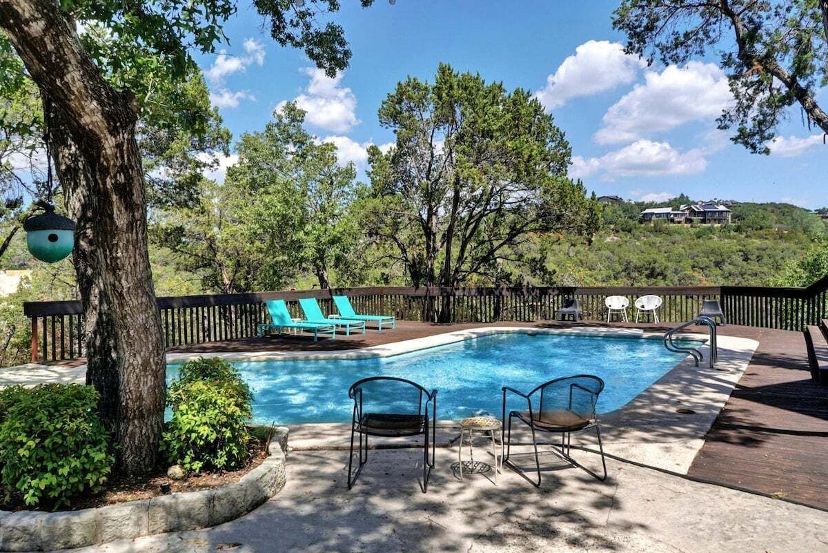 Una piscina con lettini prendisole e un solarium, circondata da alberi e una recinzione in legno.