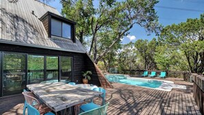 Une terrasse en bois avec une piscine, du mobilier d’extérieur et une vue sur les arbres.