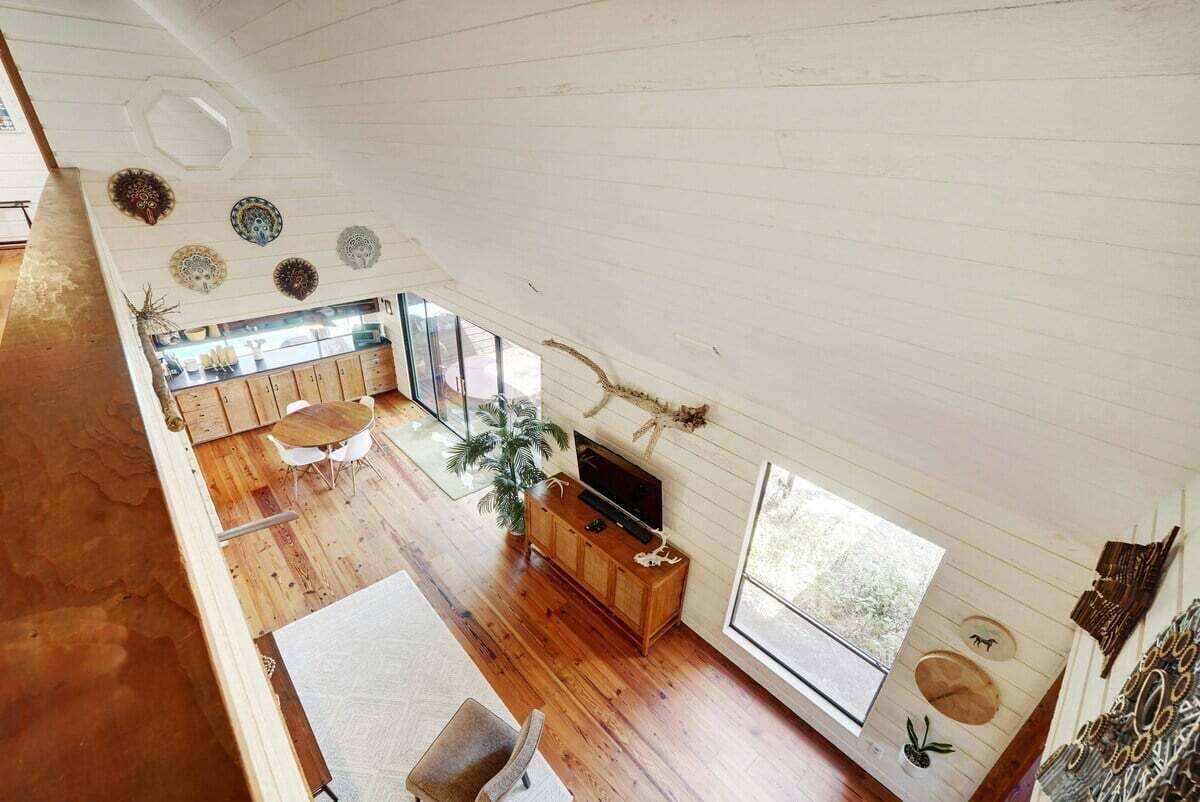 A spacious loft with high ceilings, wooden floors, a large window, and a television on a wooden cabinet.
