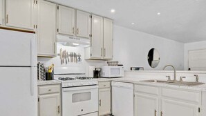 Una cocina con gabinetes blancos, estufa, microondas y fregadero.