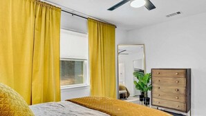Un dormitorio con cama, cortinas amarillas, cómoda y espejo.