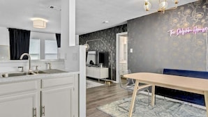 Una cocina moderna con armarios blancos, un área de comedor con mesa de madera y un letrero de neón en la pared.