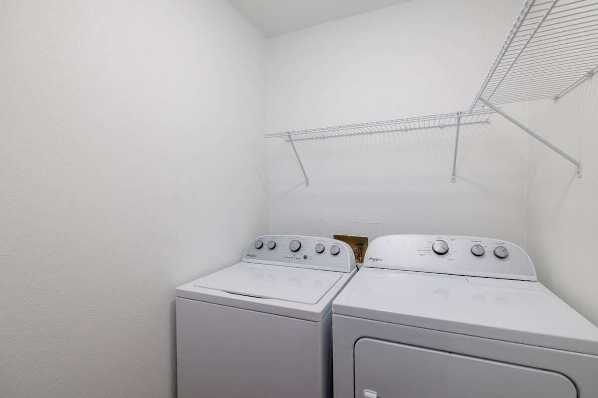 A laundry room with two stacked front-loading washing machines and a metal drying rack.
