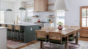 Une cuisine moderne dotée d’un îlot central, de tabourets de bar, d’une table à manger avec des chaises, d’un éclairage suspendu et de meubles de rangement en bois.