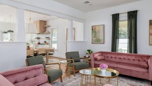 Un vaste espace de vie comprenant un canapé rose, des fauteuils verts et une table basse.