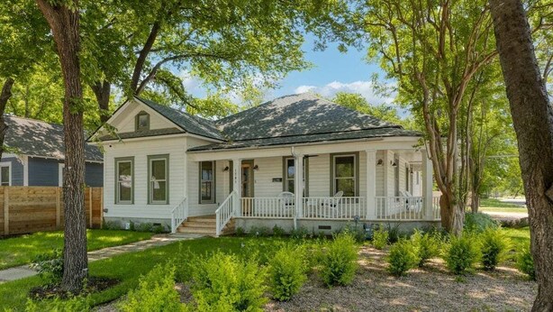 Une maison de plain-pied avec un porche à l’avant, entourée d’arbres et bordée d’une pelouse bien entretenue.