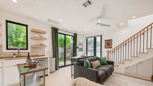 A modern interior with a kitchen, dining area, and living room, featuring a staircase, large windows, and a view of the outdoors. - 🎶 East Austin Retreat w/ Balcony + Backyard | Urban Sanctuary | Cloudscape🌮 (Austin)