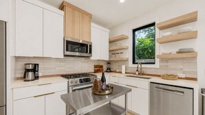 A modern kitchen with white cabinets, a stainless steel range, a microwave, and a window with a view of greenery. - 🎶 East Austin Retreat w/ Balcony + Backyard | Urban Sanctuary | Cloudscape🌮 (Austin)