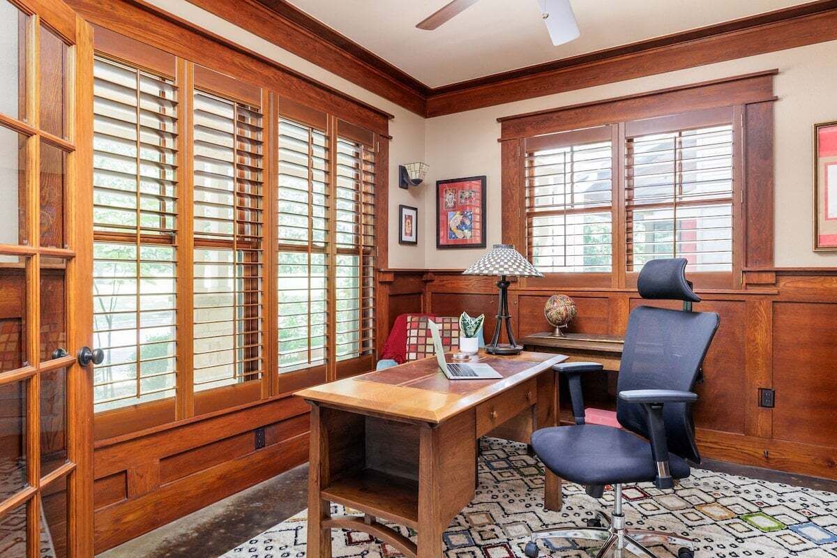 Une pièce aux murs lambrés, avec un bureau, un ordinateur portable, une chaise et une lampe.