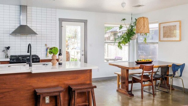 A modern kitchen with a central island, wooden bar stools, and a dining area with a table and chairs. - Downtown, UT, Walkable, East Austin Gem (Austin)