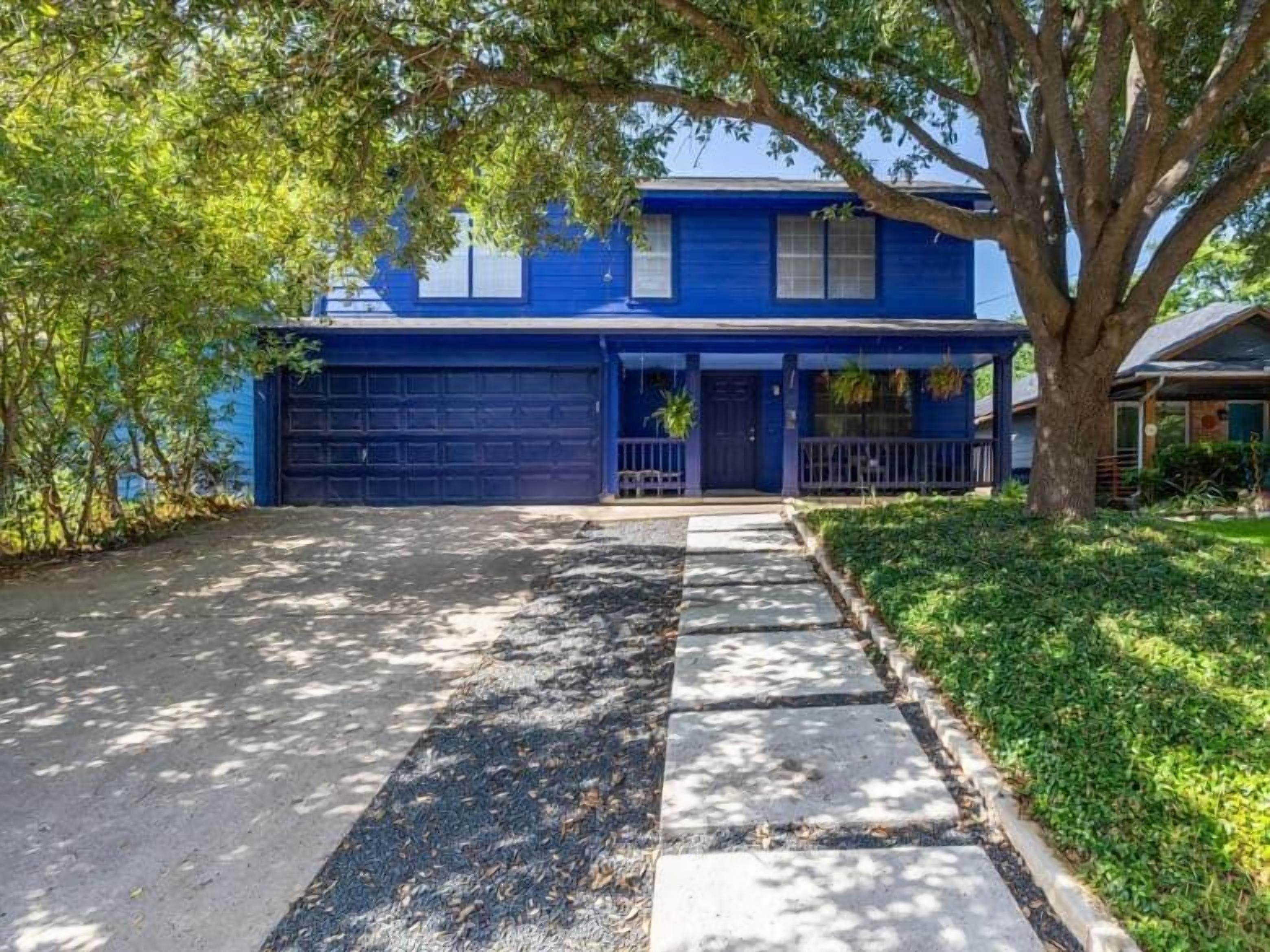 Une maison à deux étages avec une porte de garage bleue, un porche à l’avant et un arbre devant.