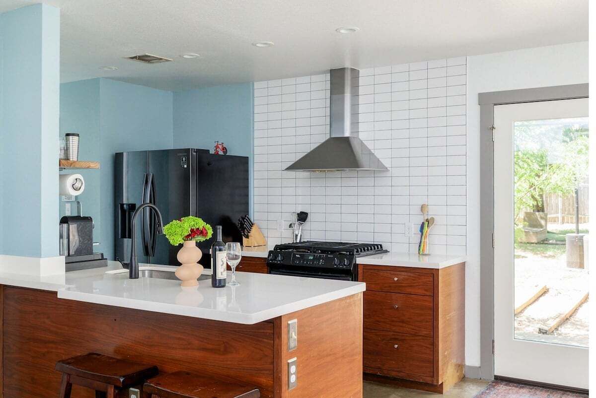 A modern kitchen with a central island, a black refrigerator, a stove, and a large window.